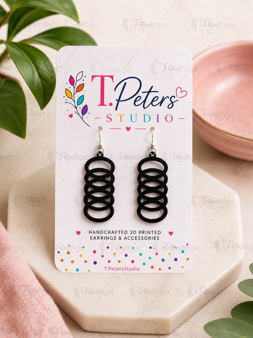 Black circular earrings on a T. Peters Studio card with a plant and pink dish in the background.